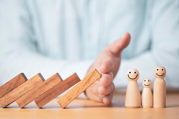 Businessman hand gesture protecting wooden domino falling to family dolls for insurance and assurance concept.