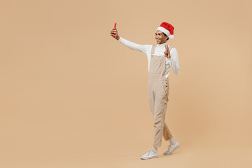 Wall Mural - Full body young african man in red Christmas hat do selfie shot mobile cell phone post photo on social network isolated on plain pastel beige background studio Happy New Year 2022 celebration concept