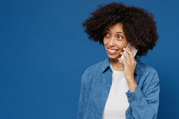 Poster - Young smiling happy black woman in casual clothes shirt white t-shirt talk speak on mobile cell phone conducting pleasant conversation isolated on plain dark blue background. People lifestyle concept.