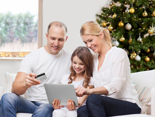 Poster - family, winter holidays and technology concept - happy mother, father and daughter with tablet pc computers and credit card shopping online at home over christmas tree lights background