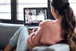 © nenetus - Back view of beautiful woman speaking on video call with diverse colleagues on online briefing with laptop on sofa at home.