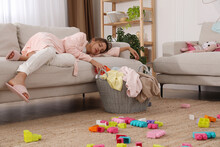 Tired Young Mother Sleeping On Sofa In Messy Living Room