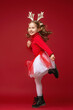 happy little girl in reindeer antlers running and jumping on red background