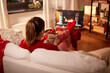 © Syda Productions - christmas, winter holidays and leisure concept - young woman watching tv with fireplace on screen and holding mug of marshmallow and whipped cream resting feet on table at cozy home