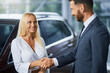 © serhiibobyk - Caucasian car dealer in stylish suit shaking hands with charming woman with blond hair after successful agreement of buying car. Concept of people, selling and purchase.