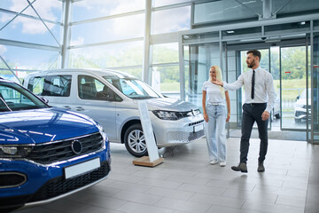 Caucasian handsome man and beautiful woman walking together at modern auto salon. Salesman helping female customer buying new transport.