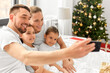 family, winter holidays and people concept - happy mother, father and two daughters with christmas gifts taking selfie in bed at home