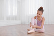 © New Africa - Little ballerina tying pointe shoes on floor in dance studio. Space for text