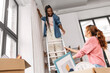 © Syda Productions - moving, home improvement and real estate concept - happy smiling women with ladder hanging curtain