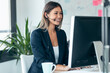 © nenetus - Attractive business woman making video call with computer while talking with earphone sitting in modern startup office.