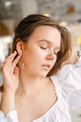 Wall Mural - A girl with dangling earrings gently straightens them with her hand on her ear