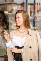 Wall Mural - A young woman in a beige raincoat stands near a shop window