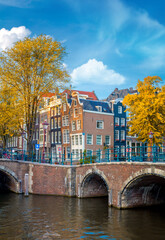 Sticker - Soul of Amsterdam is leaning houses, bridges, canals. Beautiful autumn, golden falling leaves and blue sky. Autumn day in Amsterdam. Amsterdam, Holland, Europe