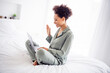© deagreez - Profile side view portrait of attractive cheerful girl sitting on bed using laptop calling video at light white home indoors