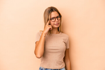 Poster - Young caucasian woman isolated on beige background pointing temple with finger, thinking, focused on a task.