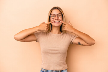 Poster - Young caucasian woman isolated on beige background smiles, pointing fingers at mouth.