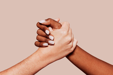 Close up multiracial woman couple with black and caucasian hands holding each other in tolerance unity love and anti racism concept. Studio shot, pastel beige background.