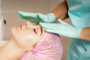 Wall Mural - The woman is having cosmetic treatment during cosmetologist in medical gloves are touching the female face at the spa salon