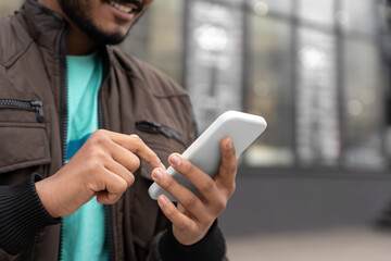 Closeup of Indian man holding mobile phone texting message standing outdoors