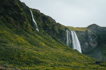 Waterfalls with mountains and green meadow on a cloudy day