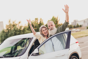 Photo of cheerful aged couple husband wife good mood waving hands hello bye ride transport car travel outdoors