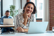 © nenetus - Smiling business woman working with laptop while looking at camera in modern startup office.