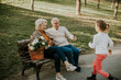 © BGStock72 - Cute little granddaughter running toward grandparents sitting on the bench in autumn park