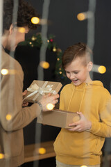 Sticker - Smiling mother opening gift box with Christmas present while showing it to son, lights effect