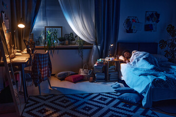 African young woman sleeping in the bed at night in her bedroom with lamp on the table