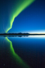 a curtain of aurora borealis or northern lights reflects in the quiet water of the kelly river in th