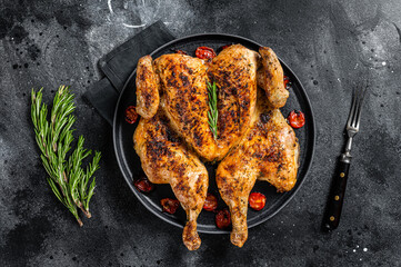 Wall Mural - Tobacco whole chicken on plate with herbs and tomato. Black background. Top view