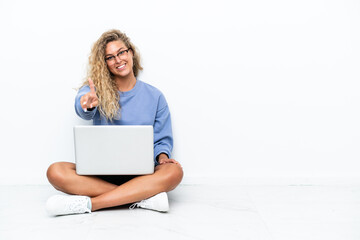 Wall Mural - Girl with curly hair with a laptop sitting on the floor showing and lifting a finger