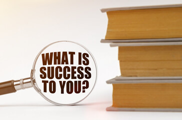 On a white background, books and a magnifying glass, inside which it is written - WHAT IS SUCCESS TO YOU