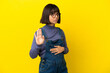 © luismolinero - Young pregnant woman over isolated yellow background making stop gesture