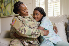 Smiling Military Woman Embracing Sad Daughter On Sofa, African American