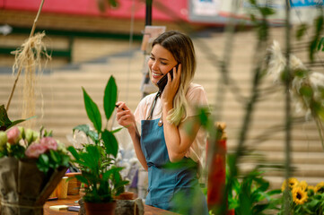 Wall Mural - Florist talking with client on the smartphone and taking an order in a flower shop