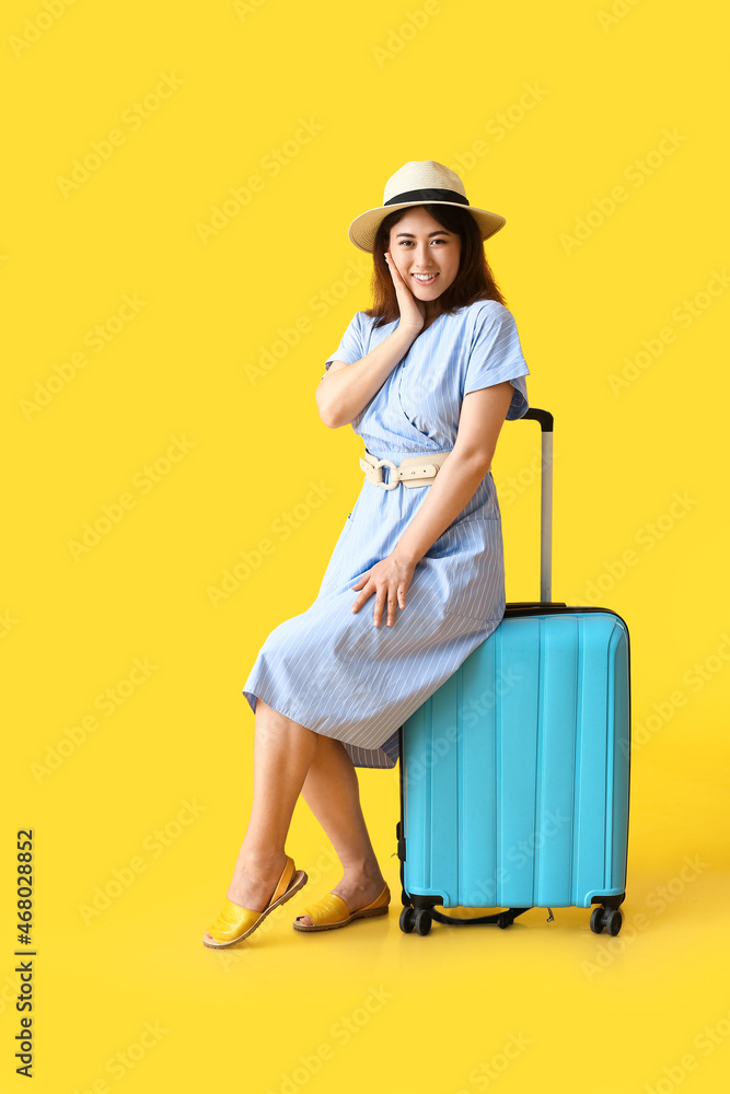 Young woman with suitcase on color background