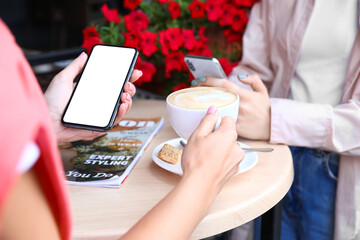 Sticker - Women using mobile phones and drinking cappuccino in cafe, closeup