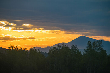 Poster - Beautiful view of a mountain range and trees under a cloudy sky at sunset