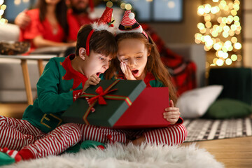 Surprised little brother and sister opening present at home on Christmas eve