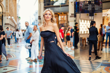 Wall Mural - Attractive young blonde girl walking in long black evening dress outdoors