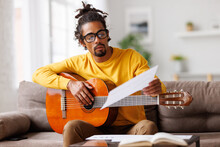 Focused African American Male Musician With Classic Acoustic Guitar Reading Sheet Music On Paper