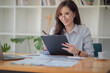 © David - Portrait of Young Asian woman hand freelancer is working her job on computer tablet in modern office. Doing accounting analysis report real estate investment data, Financial and tax systems concept.