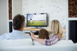 Rear view of family sitting at home together watching football match on tv