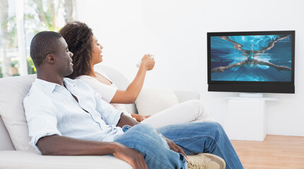 Canvas Print - Rear view of african american couple sitting at home together watching swimming competition on tv