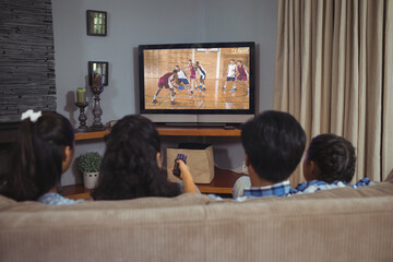 Canvas Print - Rear view of family sitting at home together watching basketball match on tv