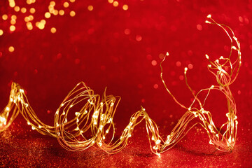 Wall Mural - Christmas background. Twisted golden xmas lights wire on sparkly festive red background. Copy space. Merry Christmas or Happy New Year card