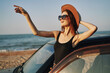 © VICHIZH - cheerful woman in sunglasses and a hat on the ocean near the car