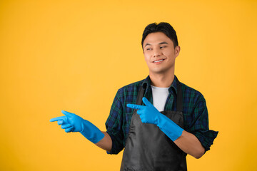 Asian young man in house cleaning clothes on yellow background He pointed his finger at the copy space on the yellow background.