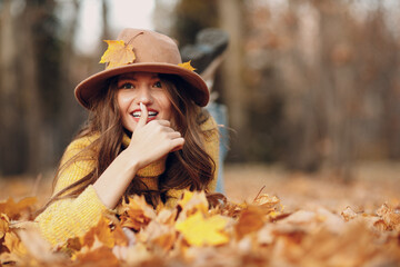 Young woman model lying in autumn park with yellow foliage maple leaves. Fall season fashion